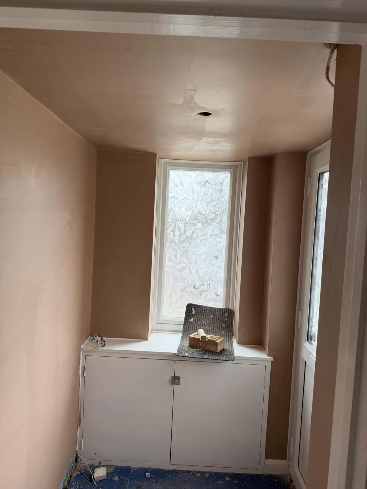 A small room skimmed floor to ceiling around a tall patterned-glass window